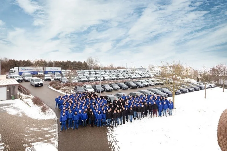 Gruppenfoto der Kratschmayer-Belegschaft in blauen Jacken auf einem verschneiten Hof vor dem Fuhrpark