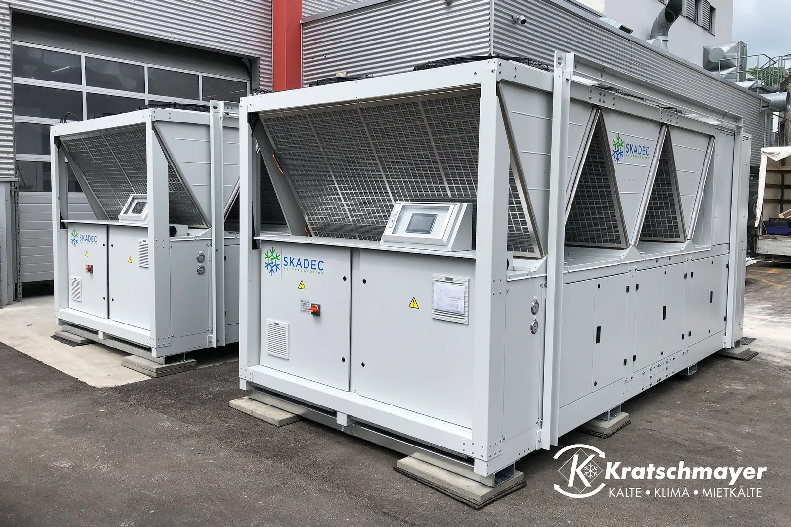 Zwei weiße Kaltwassersätze mit SKADEC-Aufschrift auf einem Hof vor einer Industriehalle