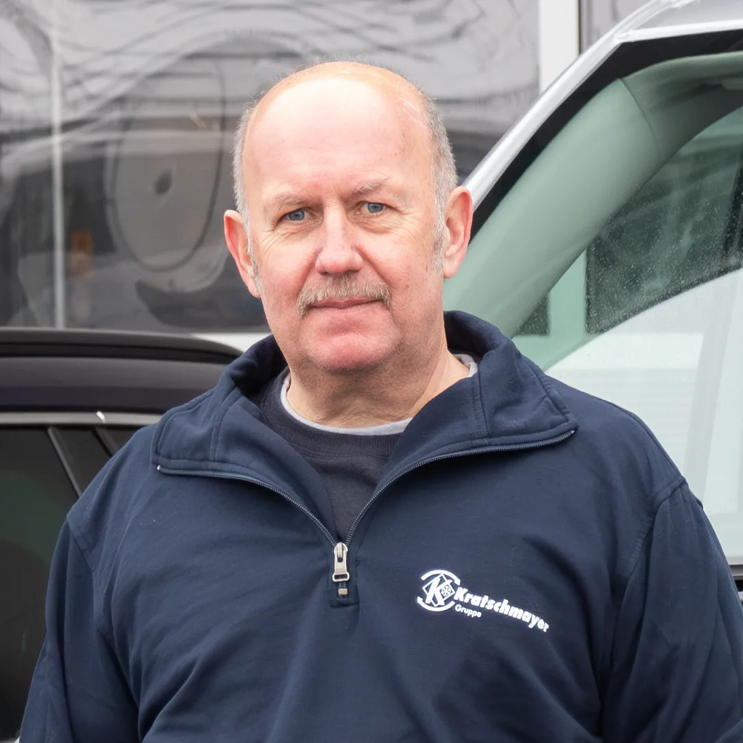 Porträt von Dirk Zerlin im dunkelblauen Kratschmayer-Pullover vor einem Firmenwagen